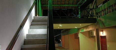 Una escalera con barandilla metálica que sube a un área del segundo piso, con paredes verdes y una puerta roja.