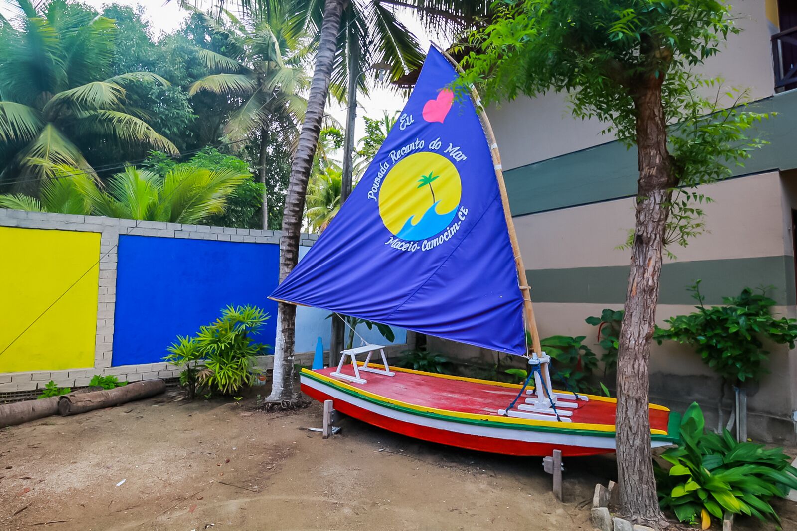 A colorful boat with a blue and yellow sail, docked near a building with a blue and yellow wall.