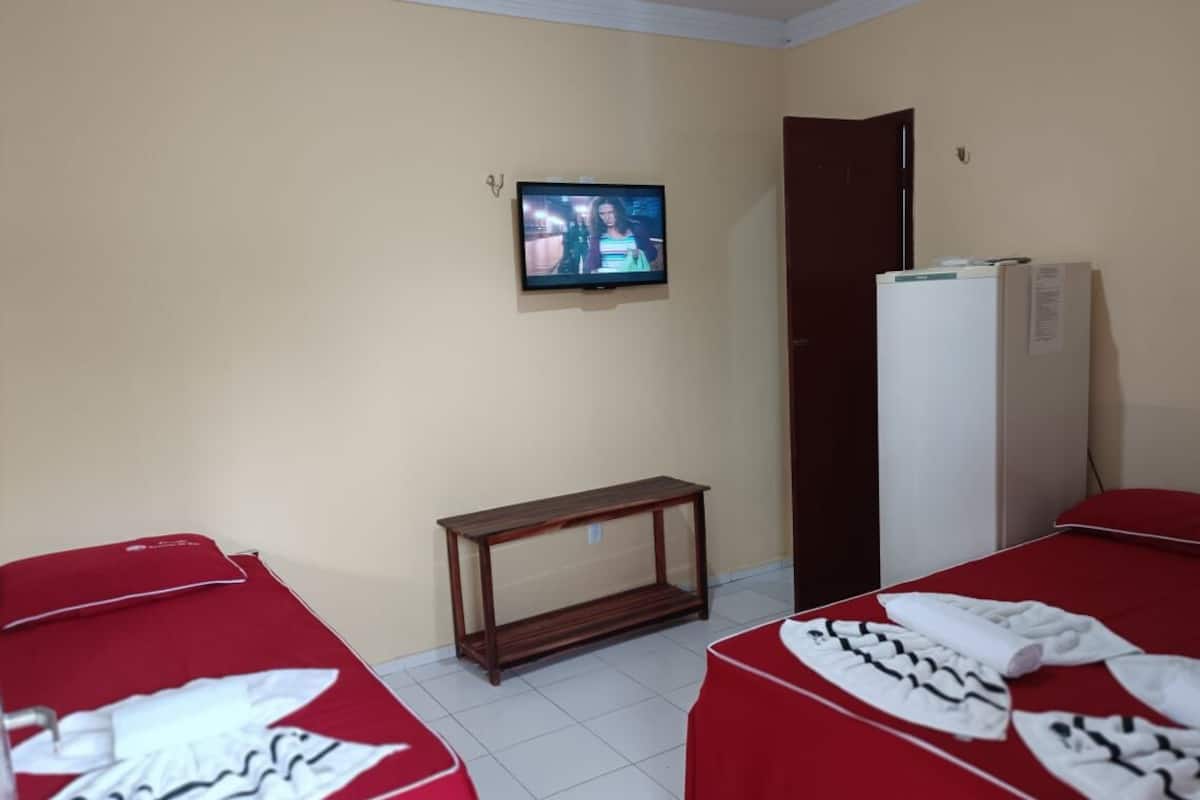 Habitación de hotel con dos camas, un televisor en la pared, una mesita y un refrigerador.