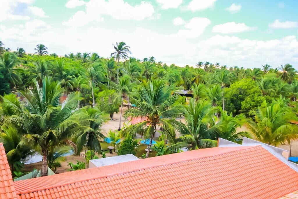 A view of a hotel with a red-tiled roof, surrounded by lush greenery and palm trees.
