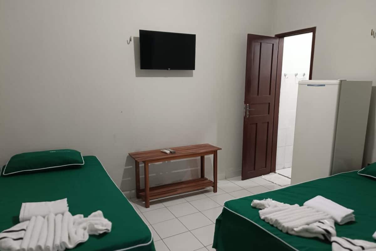 Habitación de hotel con dos camas, televisión, mesa de madera, puerta y refrigerador.
