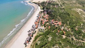 An aerial view of a coastal resort with beachfront villas, a sandy beach, and a dense green area with trees. - Pousada Recanto do Mar (Camocim)