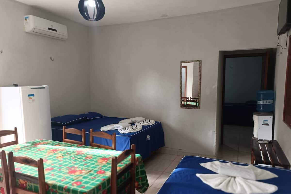 Una habitación pequeña y limpia con cama, una mesa con sillas, un refrigerador y un dispensador de agua.
