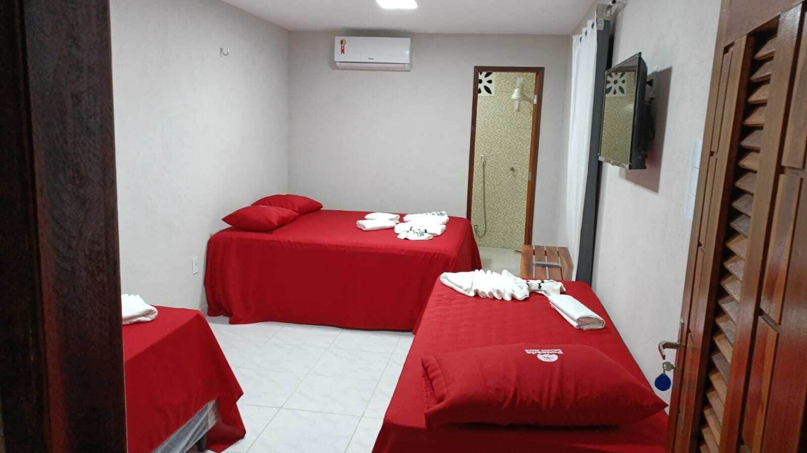 A small hotel room with two single beds, each with a red bedspread and white towels.