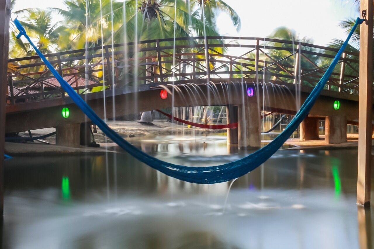 A hammock over a water feature with a bridge and palm trees in the background.