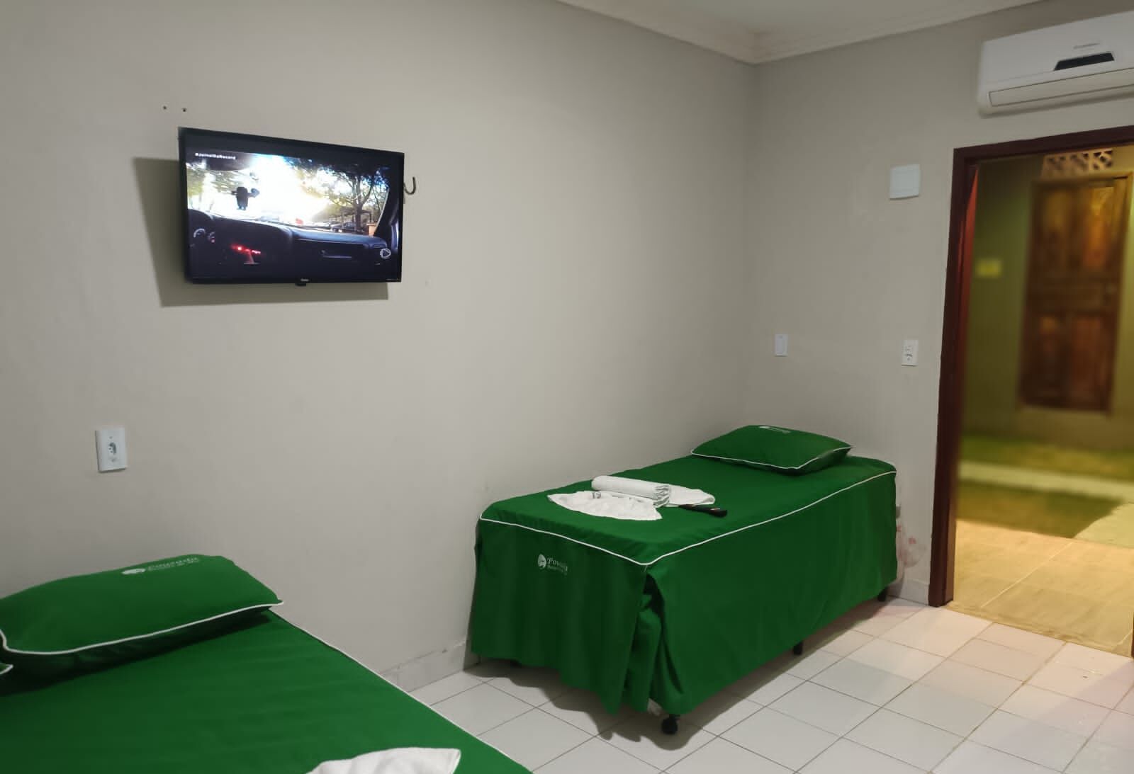A hotel room with two single beds, a television mounted on the wall, and a door leading to a corridor.