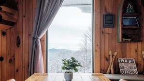 A wooden interior with a wooden table, a potted plant, a window with a view of snow-covered mountains, and a sign on the wall. - Luxe | Ski-In/Out | Hot Tub | Panoramic Views | EV (Beech Mountain)