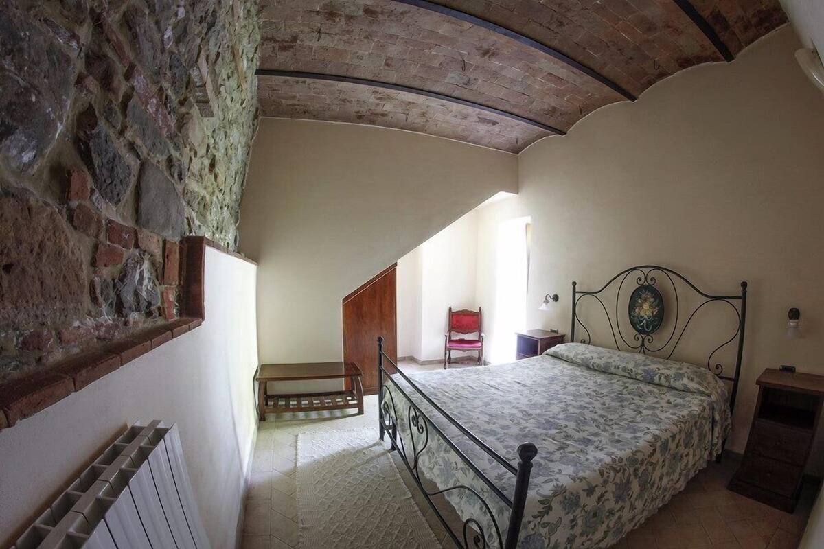 A bedroom with a bed, a chair, a wooden bench, and a radiator.