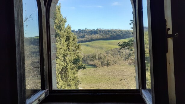 A view through an arched window of a landscape with rolling hills and trees. - Agriturismo Alle Rose (Volterra)