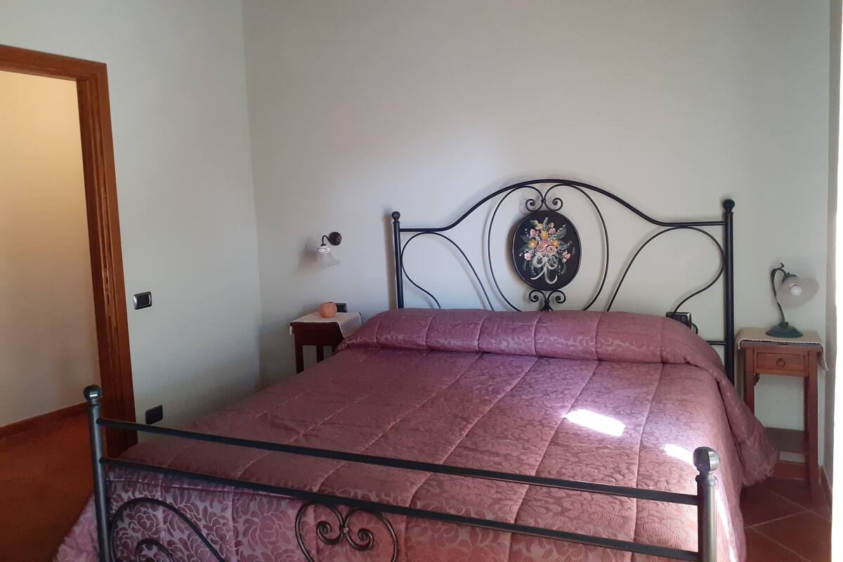 A bedroom with a metal bed frame, a wooden door, a small bedside table, and a nightstand with a lamp.