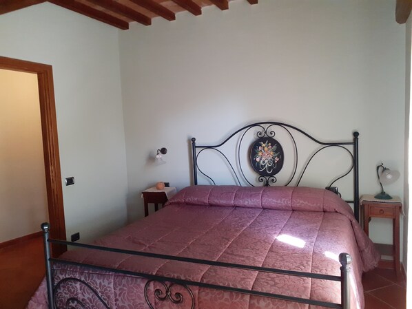 A bedroom with a metal bed frame, a wooden door, a small bedside table, and a nightstand with a lamp.