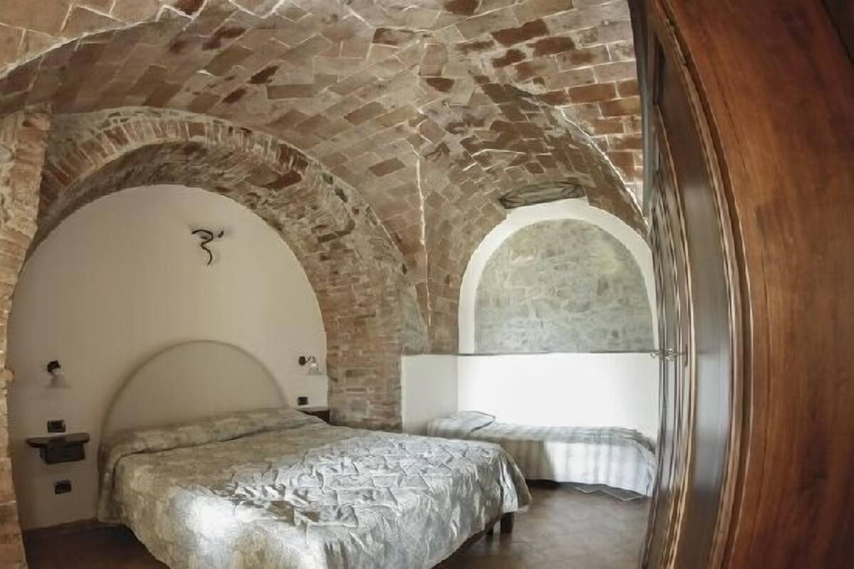 A room with a stone vaulted ceiling, a bed with a headboard, and a bedside table.