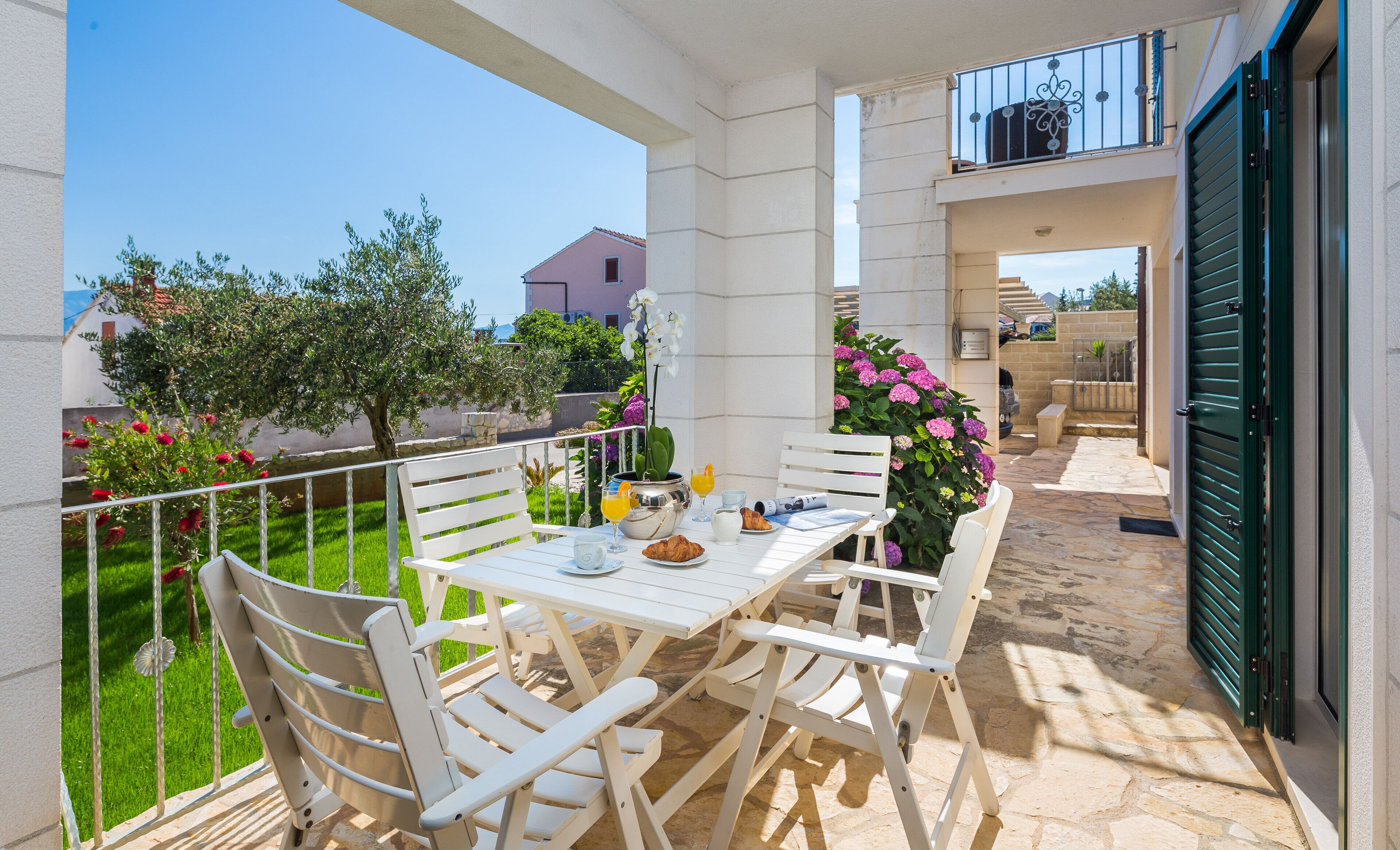 Un balcon avec une table préparée pour le petit-déjeuner, comprenant des croissants et du jus d’orange, entouré de chaises blanches.