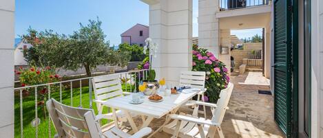 Un balcon avec une table préparée pour le petit-déjeuner, comprenant des croissants et du jus d’orange, entouré de chaises blanches.