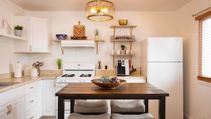 A modern kitchen with white cabinets, a wooden dining table, and two chairs. There is a white refrigerator, a stove, and a coffee maker on the counter. - Lake Erie House Near Cedar Point & The Beach (Huron)