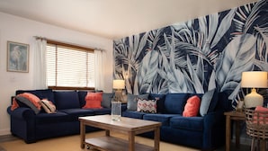 A living room with a dark blue sofa, a wooden coffee table, and a large tropical leaf-patterned wall. - Lake Erie House Near Cedar Point & The Beach (Huron)