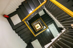 A spiral staircase with black and yellow railings, a framed picture on the wall, and a red object on the left.