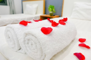 A neatly folded white towel with red rose petals on a bed in a hotel room.