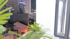 A balcony with potted plants, a glass door, and a view of city buildings at night. - T P Luxury House (Da Nang)