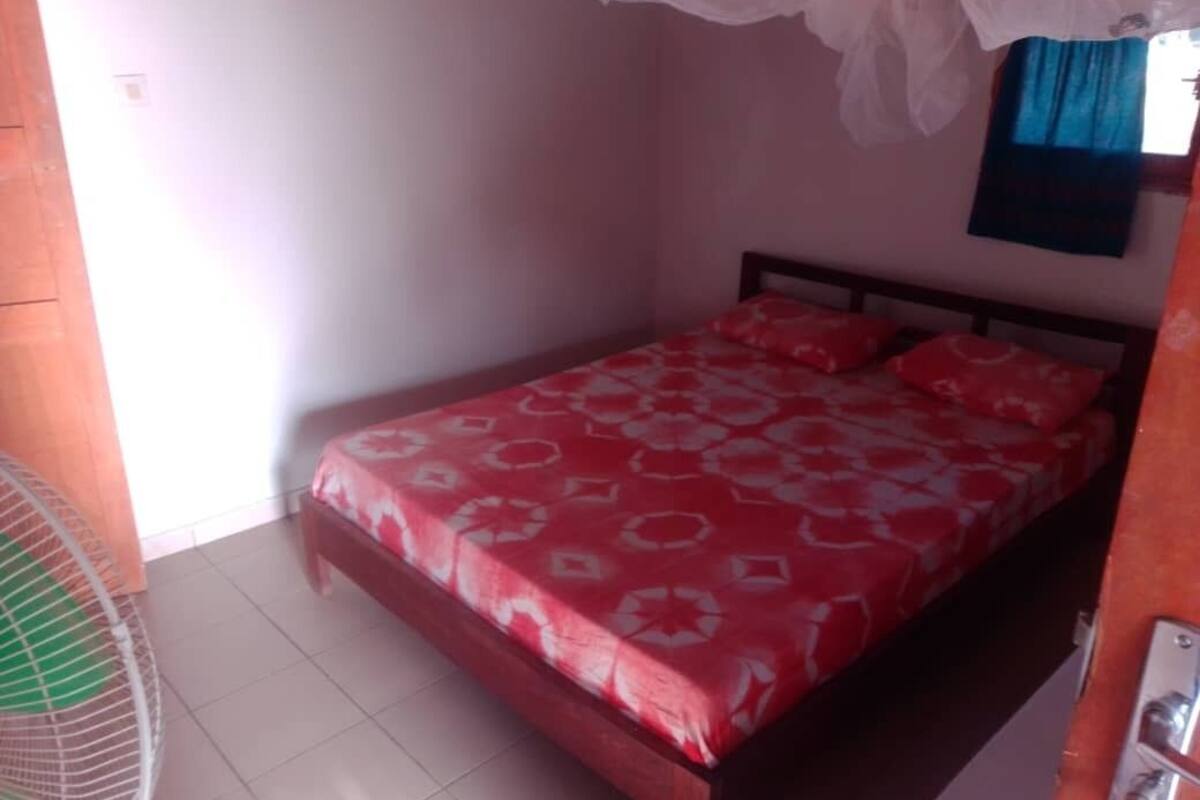 Une chambre à coucher avec un lit, un ventilateur et une fenêtre avec des rideaux.