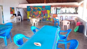 A room with a long blue table and matching chairs, a mural on the wall, and a thatched roof ceiling.