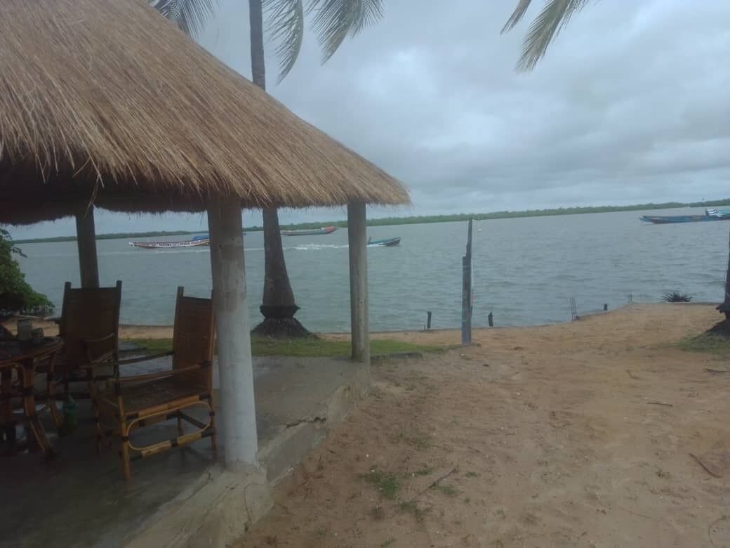 Ett område vid stranden med en byggnad med halmtak, trästolar och en sandstrand.