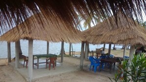 A beachside area with thatched-roof structures, tables, and chairs.