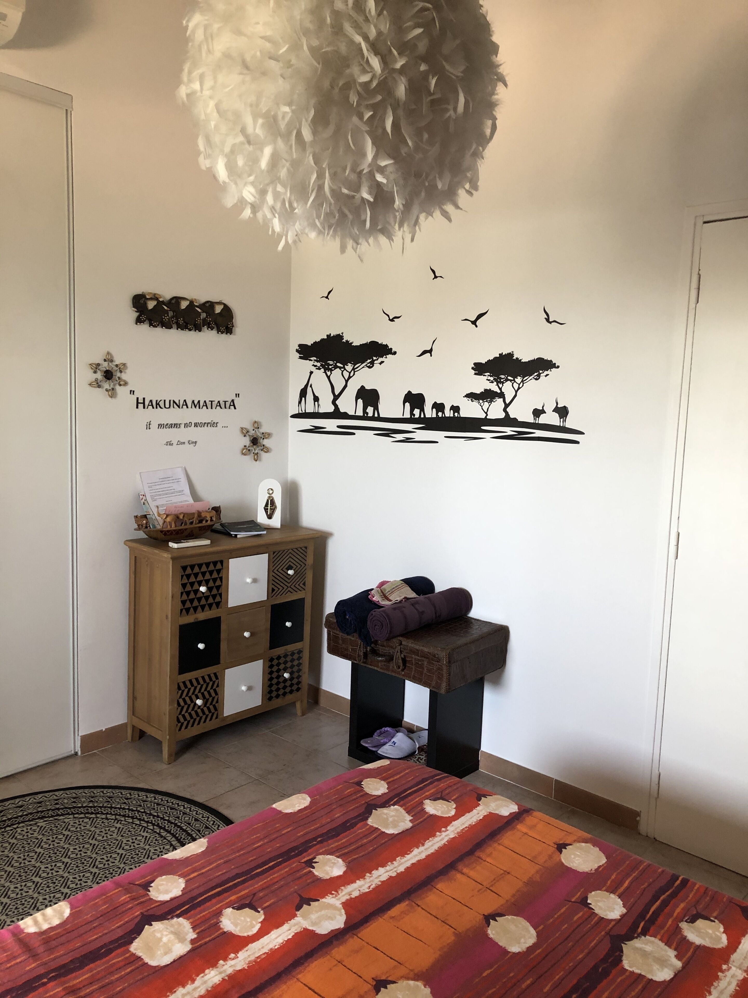 A room with a bed, a wooden cabinet, a wall decal, and a hanging light fixture.