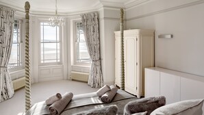 A bedroom with a four-poster bed, a white wardrobe, and a view of the sea through large windows. - 5* luxury pet friendly house in Woolacombe with hot tub and sea views (Woolacombe)