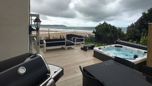 A deck with outdoor seating, a hot tub, and a view of the beach. - 5* luxury pet friendly house in Woolacombe with hot tub and sea views (Woolacombe)