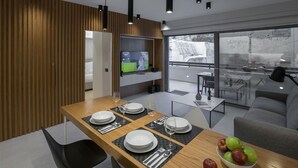 Ein moderner Essbereich mit einem Holztisch, gedeckt für vier Personen, einem an der Wand montierten Fernseher und einem Balkon mit Blick auf die Stadt.