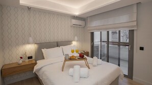 Ein modernes Hotelzimmer mit einem großen Bett, einem Nachttisch mit Lampe, einer Ablage mit Handtüchern und Frühstücksangeboten und einer Schiebeglastür nach draußen.