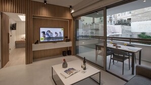Ein modernes Wohnzimmer mit Fernseher, Couchtisch mit einer Zeitschrift und Glastisch mit Flasche und Glas.
