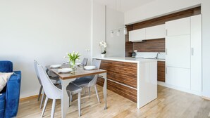Une cuisine moderne avec des meubles blancs, un mur d’accent en bois et un coin repas avec une table dressée pour quatre personnes.