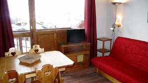 A cozy room with a wooden dining table, chairs, a red sofa, a TV, and a small shelf. - 20m from ski slopes, 4th floor, view ski slopes, 42m², La Plagne (La Plagne)