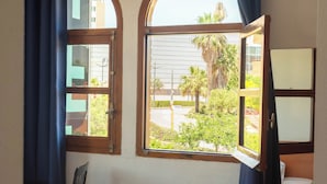 Um quarto com uma cama, uma janela com cortinas, uma mesinha e vista para o exterior.