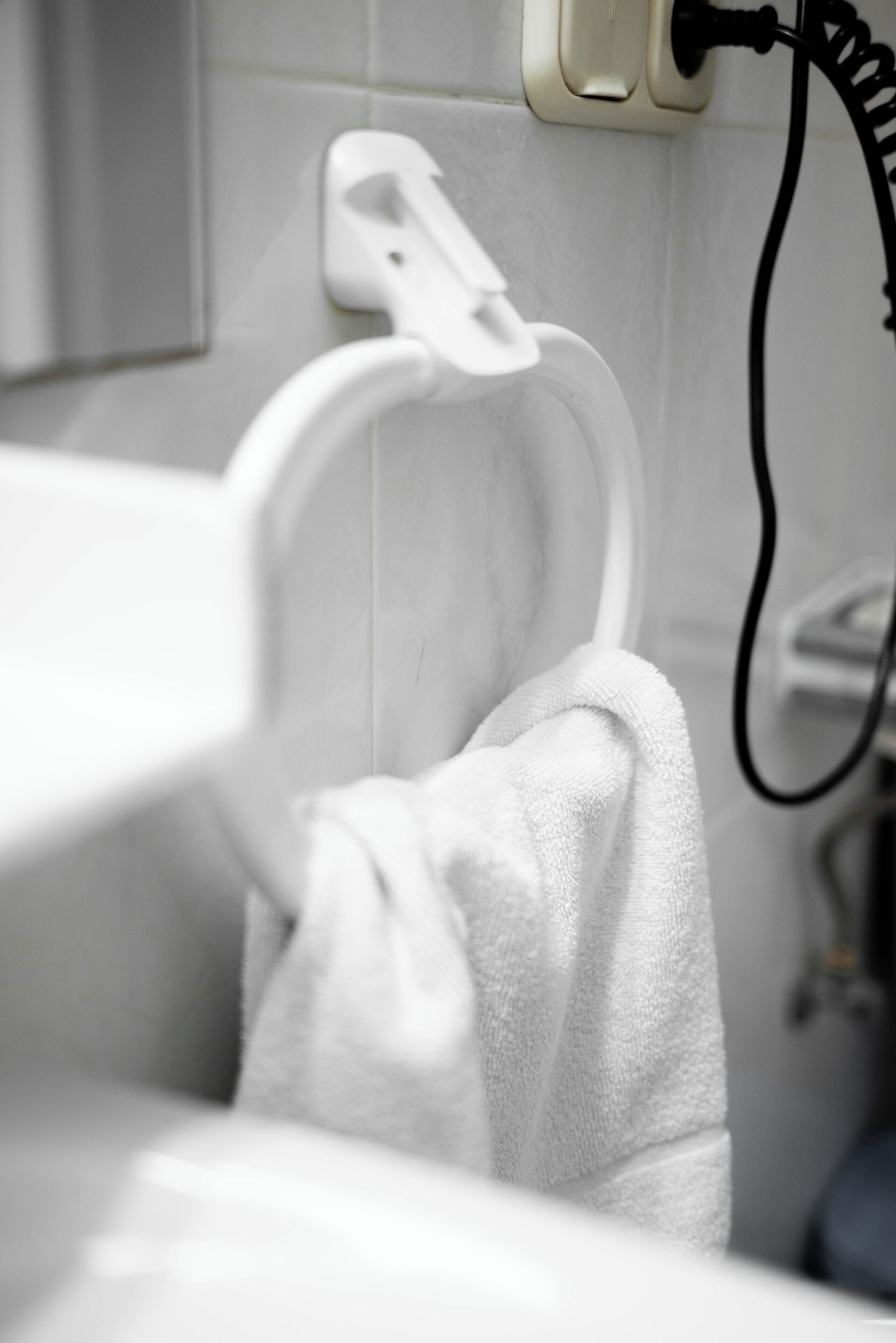 Un baño con un perchero, una toalla blanca colgada, un enchufe y un cable de carga negro.