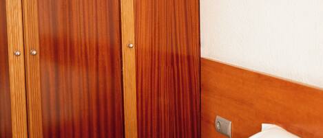 A hotel room with a wooden wardrobe, a bed with white bedding, and a wall-mounted light switch.