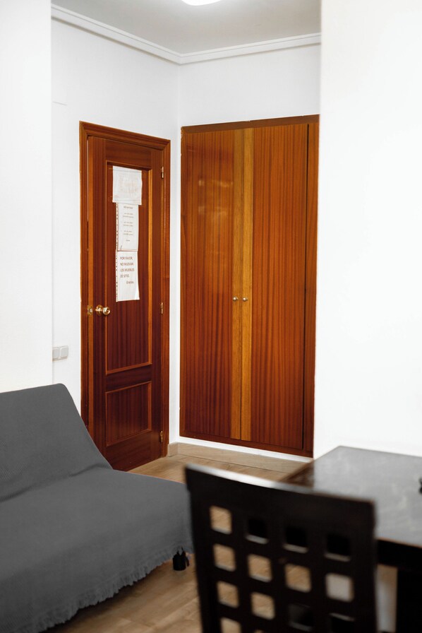 A room with a wooden wardrobe, a grey sofa, and a dining table. - Hotel Sundos Feria Valencia (Valencia)