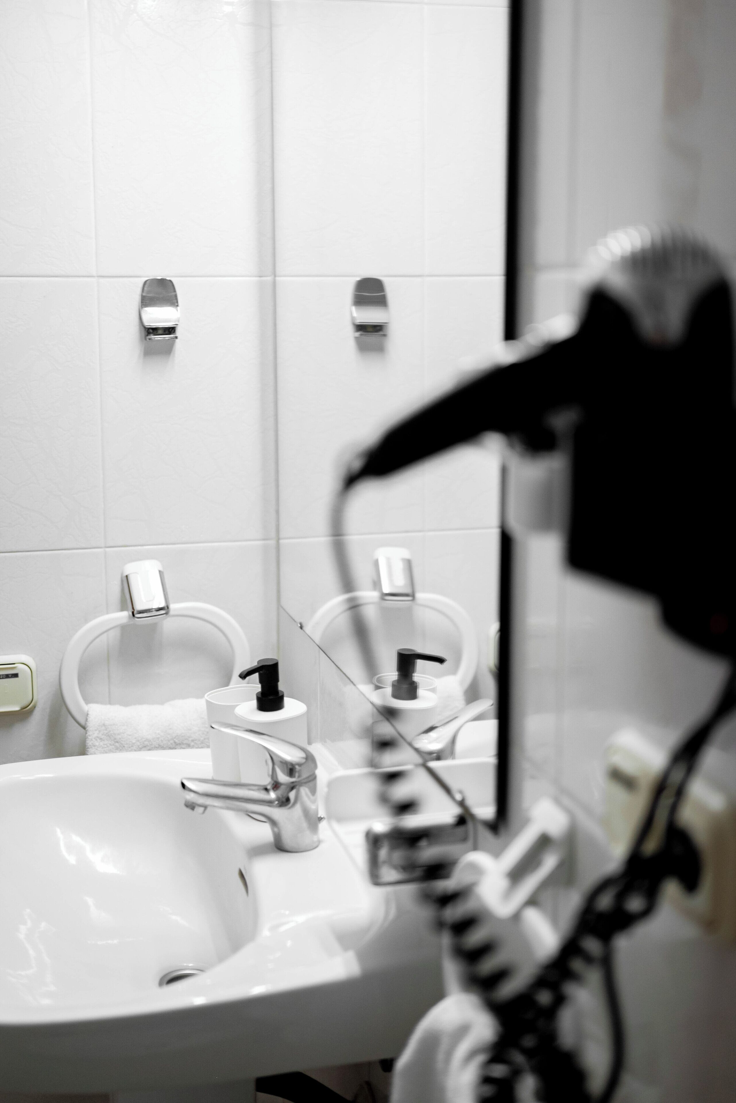 Casa de banho com lavatório branco, dois suportes para toalhas, espelho e secador de cabelo.