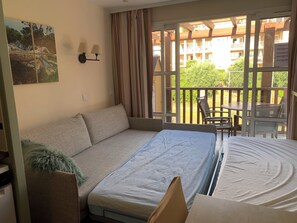 A room with a sofa bed, a small table with chairs, a balcony with a view of buildings and greenery, and a painting on the wall. - Cap Esterel 2P Sea view 5Pers. Air-conditioned (Saint-Raphaël)