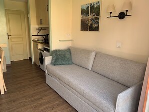 A living room with a sofa, a kitchen in the background, and a wall-mounted lamp. - Cap Esterel 2P Sea view 5Pers. Air-conditioned (Saint-Raphaël)