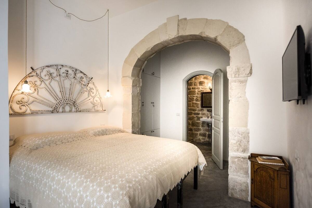 Un dormitorio con cama, un adorno en la pared, un arco y una pared de piedra.