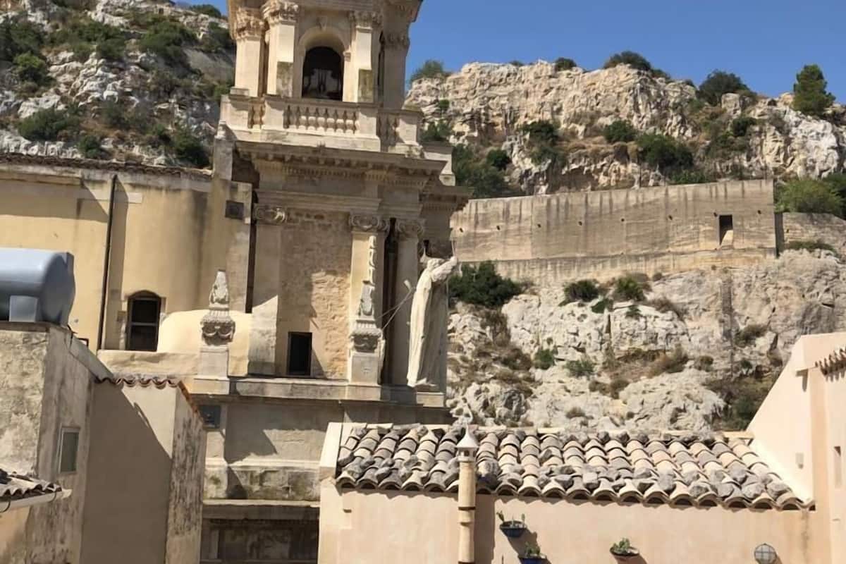 Un edificio con cúpula y campanario, rodeado de terreno pedregoso y vegetación.