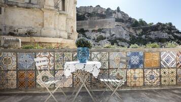 Un mur recouvert de carreaux, avec une petite table et un banc, un vase décoratif et, au fond, une colline rocheuse.