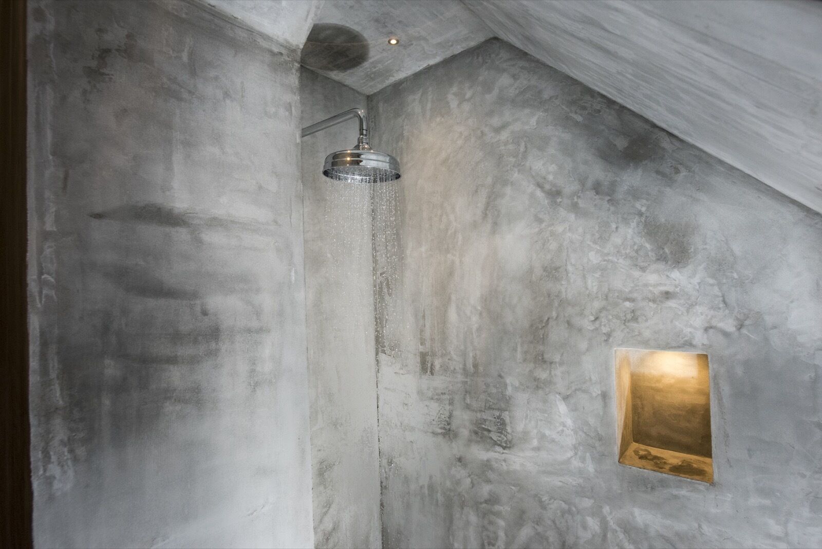 A shower with a modern design, a textured wall, and a small illuminated panel.