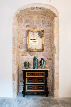 A stone wall with a framed picture and three vases on a black dresser. - Sanbartolomeo Casa e Putìa (Scicli)
