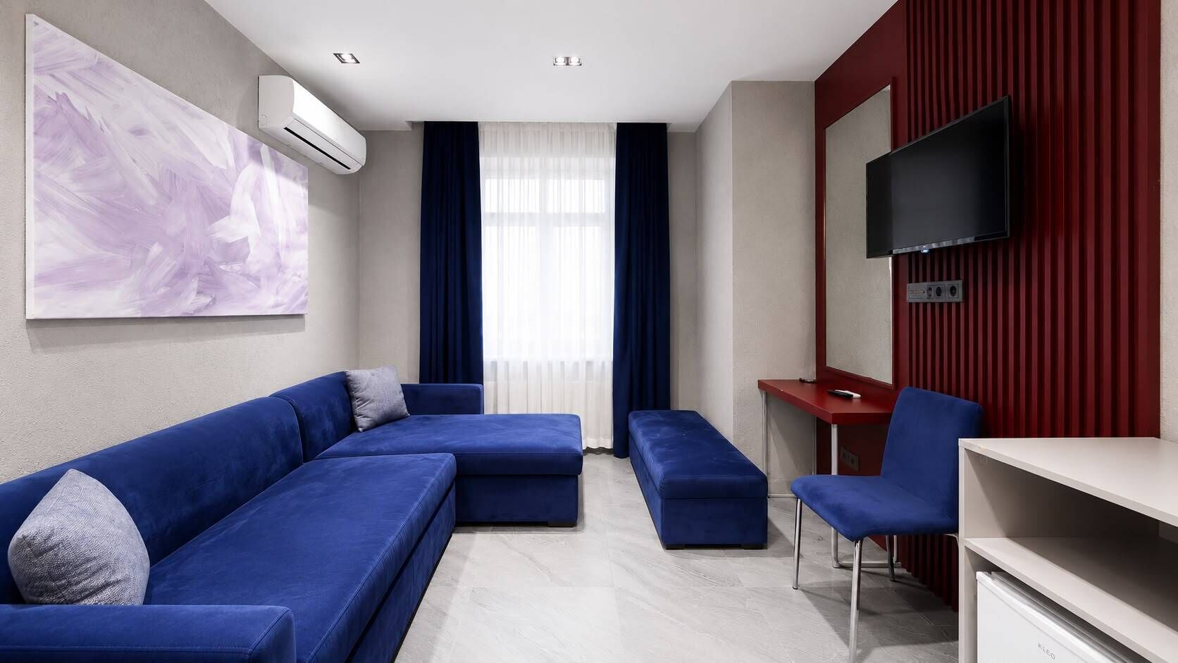 A modern living room with a sectional sofa, a small table, a chair, and a flat-screen TV mounted on a red wall.