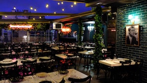 A restaurant with multiple tables and chairs, a neon sign, and a brick wall with a framed picture. - Voir Hotel Pera (Istanbul)