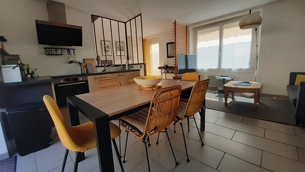 Een moderne keuken met een eethoek, met een houten tafel, rieten stoelen en een groot raam dat natuurlijk licht binnenlaat.